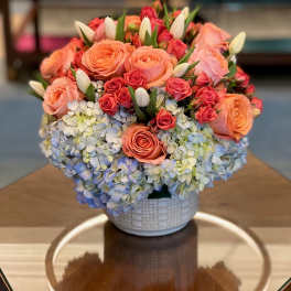 Peach and pink roses with blue hydrangeas in a white vase