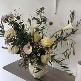 White floral arrangement in a cream vase with calla lilies and ranunculus