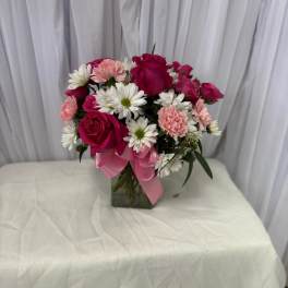 Pink roses and white daisies arranged in a glass vase with a pink ribbon