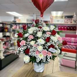 Red heart balloon above a vase of red, white, and pink flowers