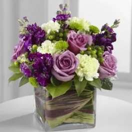 Purple and white floral arrangement in a square glass vase