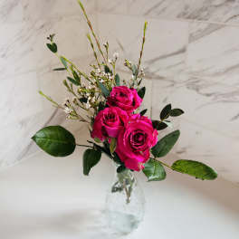Three hot pink roses in a clear glass vase with small white filler flowers