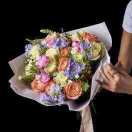 Hand-tied bouquet of pastel roses and purple blooms in white wrap