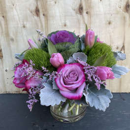 Pink roses and tulips arranged in a glass vase with silver foliage