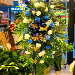 Tall floral standing spray with blue and white flowers and butterfly accents