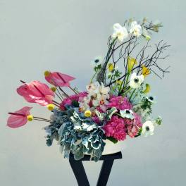 Pink and white floral arrangement in a white vase on a black stand