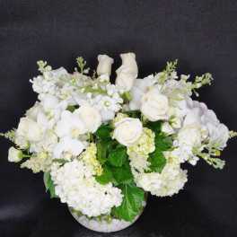 White roses and orchids arranged in a round glass vase