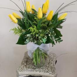 Yellow tulips arranged in a clear glass vase with a white ribbon