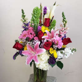 Tall mixed bouquet in a clear glass vase with pink lilies and red roses