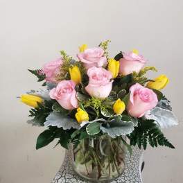 Pink roses and yellow tulips arranged in a clear glass vase