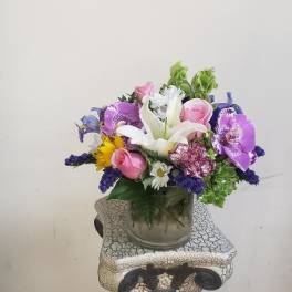 Mixed bouquet with white lilies, pink roses, and purple orchids in a glass vase