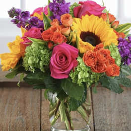 Mixed bouquet of roses, sunflowers, and purple blooms in a glass vase