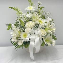 White floral arrangement with lilies, roses, and daisies in a round container