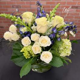 Cream roses and blue flowers arranged in a glass vase