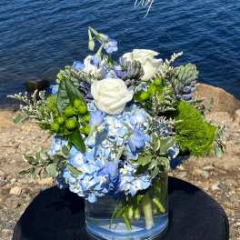 Blue and white floral arrangement in a glass vase by the water