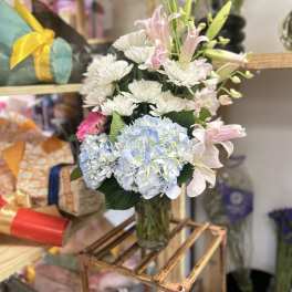 Mixed bouquet of lilies, hydrangeas, and white daisies in a glass vase