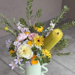 Mixed bouquet in a mint vase with yellow, pink, and lavender blooms