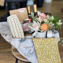 Gift basket with flowers, wine bottles, candles, and a knitted item
