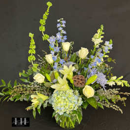 Tall floral arrangement in a glass vase with white roses, blue flowers, and lilies