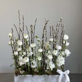 White floral arrangement with tall pussy willow branches in a rectangular container
