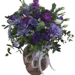Purple floral arrangement in a round glass vase with a ribbon bow