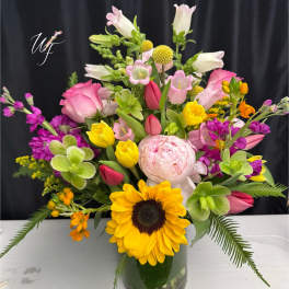 Mixed bouquet with sunflowers, pink roses, and tulips in a glass vase