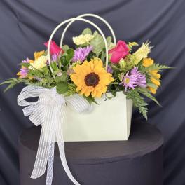 Mixed flower arrangement in a white handled gift bag with a ribbon bow