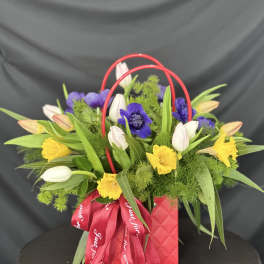 Mixed bouquet in a red handled gift bag with a red ribbon
