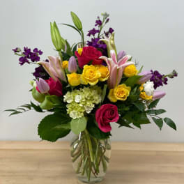 Mixed bouquet of roses, lilies, and purple flowers in a glass vase