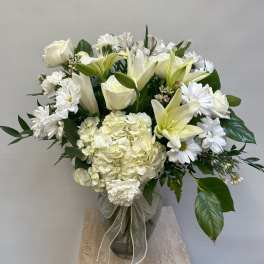 White roses, lilies, and daisies arranged in a glass vase with a ribbon.