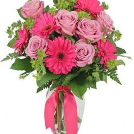 Pink roses and gerbera daisies in a glass vase with a ribbon