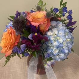 Bouquet of orange, blue, and purple flowers in a vase with ribbon