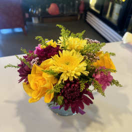 Mixed bouquet of yellow, pink, and purple flowers in a glass vase