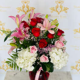Bouquet of red and pink roses with lilies in a red glass vase