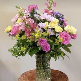 Mixed pink, yellow, and purple flowers in a clear glass vase