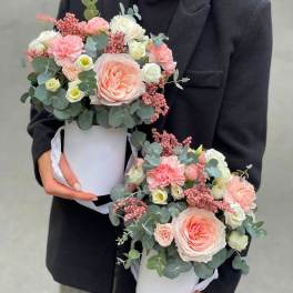 Two pastel flower arrangements in white hat boxes held by a person