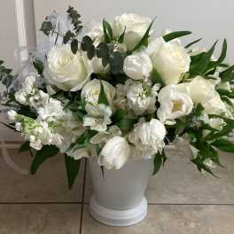 White floral arrangement in a white pedestal vase with green foliage