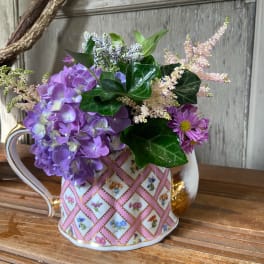 Purple hydrangea and daisy bouquet in a patterned teacup vase