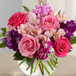 Pink roses and purple flowers arranged in a clear glass vase