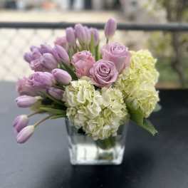 Lavender tulips and roses with pale hydrangeas in a clear glass vase