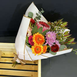Mixed bouquet with orange daisies, pink roses, and purple blooms in white wrap