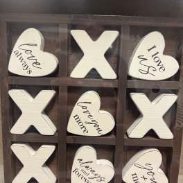 Wooden tic-tac-toe sign with heart and X pieces reading love phrases