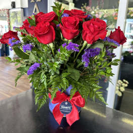 Bouquet of red roses with purple filler in a blue hatbox tied with a red ribbon