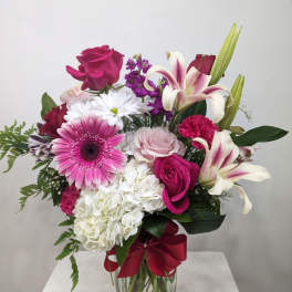 Mixed bouquet of pink and white flowers in a glass vase with a red ribbon