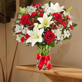 Red roses and white lilies arranged in a clear glass vase with a red ribbon