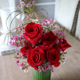 Red roses arranged in a green glass vase with small pink filler flowers