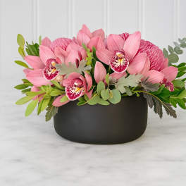 Pink orchid arrangement in a black bowl vase