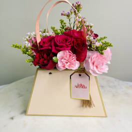 Pink and red rose arrangement in a cream gift bag with ribbon handles