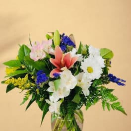Mixed bouquet of lilies, daisies, and blue flowers in a glass vase