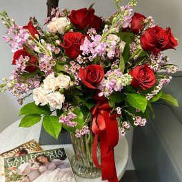 Red and blush rose bouquet in a glass vase with a red ribbon